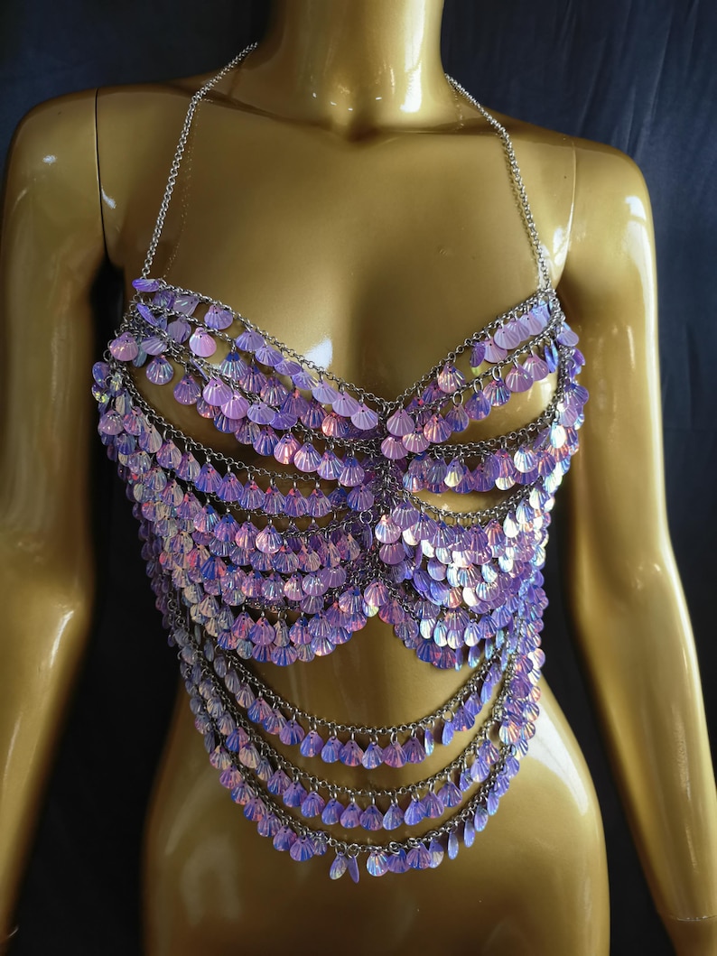 May include: A halter-style body chain top constructed from silver-toned metal links. The garment features multiple cascading rows of iridescent, light purple, shell-shaped sequins that shimmer with a pearlescent finish across the chest and torso.