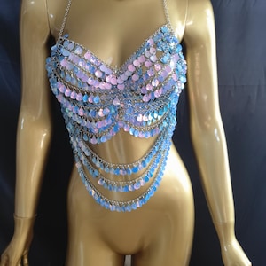 May include: A halter-style body chain top constructed from silver-toned metal links and iridescent, light-reflecting circular sequins in shades of pastel blue and pink. The garment features a multi-layered draped design that hangs from the chest.