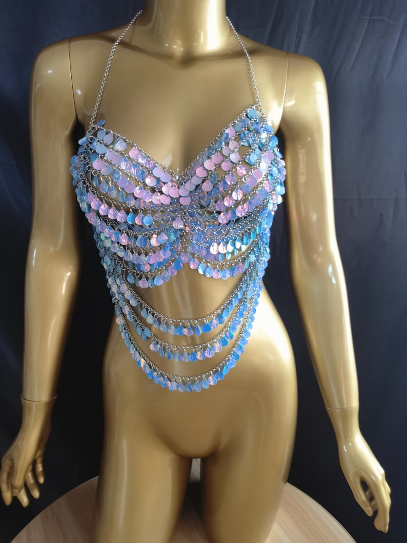 May include: A halter-style body chain top constructed from silver-toned metal links and iridescent, light-reflecting circular sequins in shades of pastel blue and pink. The garment features a multi-layered draped design that hangs from the chest.
