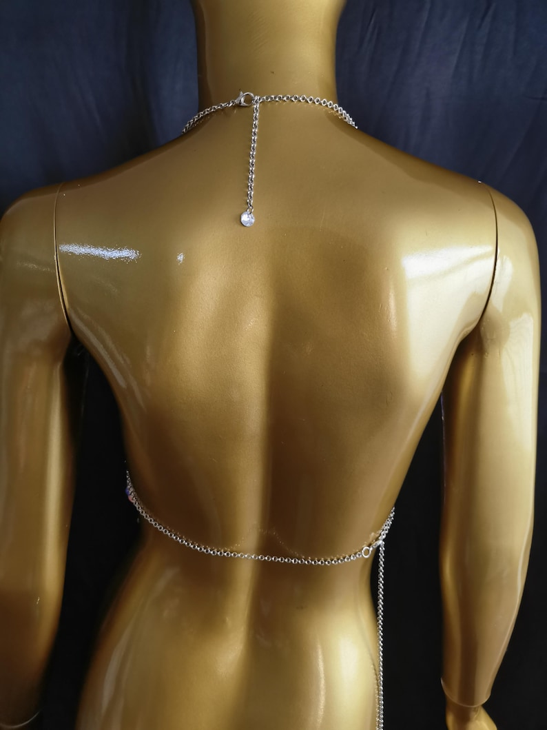 May include: A silver-toned body chain featuring a delicate link construction that wraps around the torso. The piece includes a necklace-style chain around the neck with a small circular charm at the end of the adjustable extender chain.