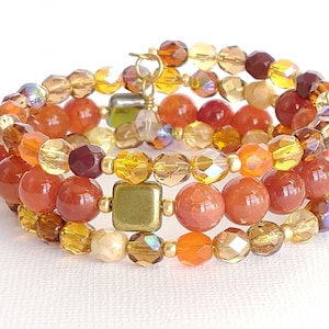 May include: A multi-strand bracelet featuring a mix of orange, brown, and gold beads. The bracelet is made with round, faceted glass beads and larger, round, opaque orange beads.