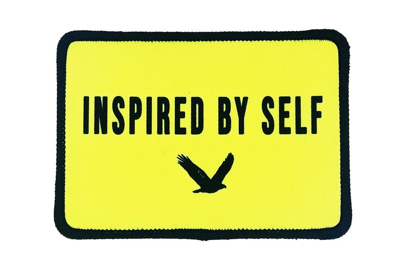 Yellow rectangle patch with bold black text reading “Inspired By Self” and a flying bird graphic, custom printed with iron-on backing.