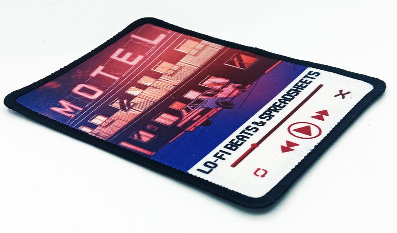 Angled side view of a full-color printed rectangle patch featuring a motel illustration and text reading “Lo-Fi Beats & Spreadsheets.”