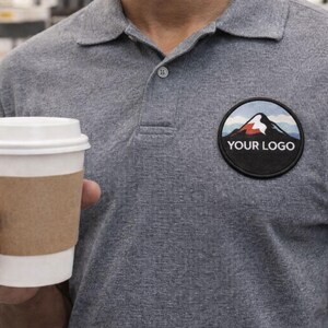 Custom round logo patch applied to a gray work polo shirt, demonstrating professional uniform branding with an iron-on patch.