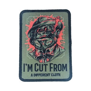 Custom rectangle patch with character artwork and the phrase “I’m Cut From a Different Cloth,” sublimated on green fabric with black border.