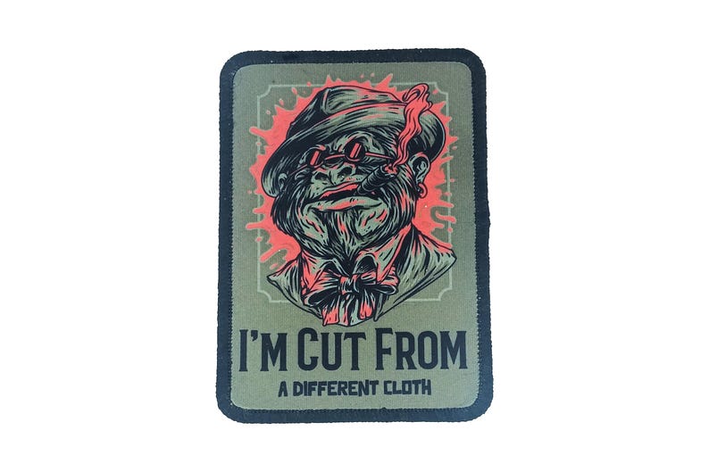 Custom rectangle patch with character artwork and the phrase “I’m Cut From a Different Cloth,” sublimated on green fabric with black border.