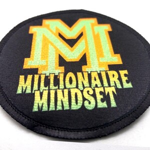 Round iron-on patch laying flat display vibrant artwork that includes text that reads "Millionaire Mindset" in lime and green with yellow outlines. The background of the patch is black.
