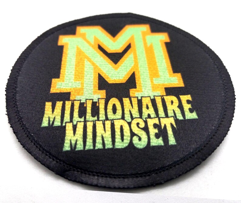 Round iron-on patch laying flat display vibrant artwork that includes text that reads "Millionaire Mindset" in lime and green with yellow outlines. The background of the patch is black.