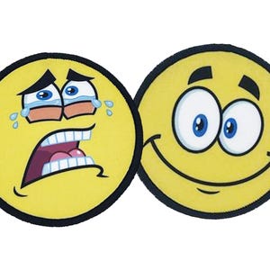 Two round iron-on patches with yellow emoji faces, one crying and one smiling, showing full-color sublimation printing and black stitched borders.
