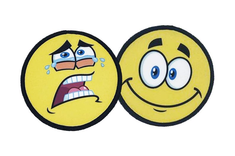 Two round iron-on patches with yellow emoji faces, one crying and one smiling, showing full-color sublimation printing and black stitched borders.