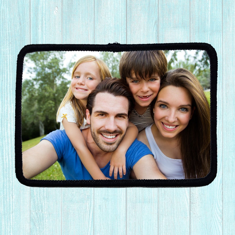 A rectangular photo with a black border. The photo features a family of four smiling at the camera. The background is a blurred green landscape.