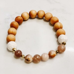 May include: A wooden beaded bracelet with brown and white beads, and pink and brown gemstone beads. The bracelet has gold accents.