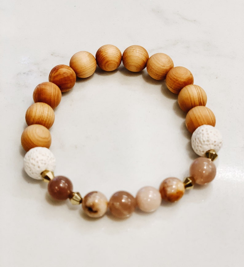 May include: A wooden beaded bracelet with brown and white beads, and pink and brown gemstone beads. The bracelet has gold accents.