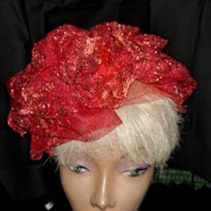 May include: A red and white hat with a large, ruffled, red fabric flower on top. The hat is made of a sheer fabric and has a white feather trim.