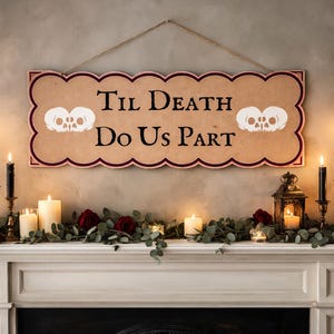 Może przedstawiać: Ozdobny szyld z napisem "Til Death Do Us Part" i grafiką czaszek. Wisi nad kominkiem ozdobionym świecami, zielenią i czerwonymi różami, tworząc gotycki lub halloweenowy motyw.