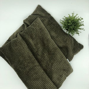 May include: A green corduroy neck wrap or neck pillow. The neck wrap is folded in half and is lying on a white surface.