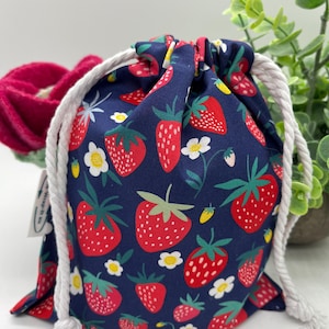 May include: A blue drawstring bag with a white cord. The bag is covered in a pattern of red strawberries and white flowers.