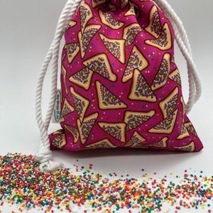 May include: A drawstring bag with a bright pink background, patterned with toast slices and colourful sprinkles. The bag has a white rope drawstring and the text "Re-Wrap-It.au" on the side. A pile of colourful sprinkles is scattered in front of the bag.