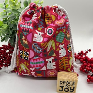 May include: A red drawstring bag featuring a Christmas-themed pattern with koalas and ornaments. The bag has a white rope drawstring. A wooden block with the words "peace & joy" is also visible.