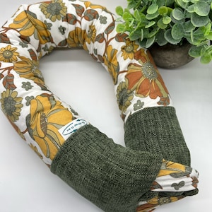 May include: A green and white floral patterned neck pillow with a green fabric back. The pillow has a label that says "Wrap It Up".