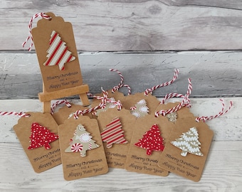 May include: Kraft paper gift tags with red and white twine. Each tag features a decorative Christmas tree and the text "Merry Christmas and a Happy New Year". The trees have various patterns, including stripes and polka dots.