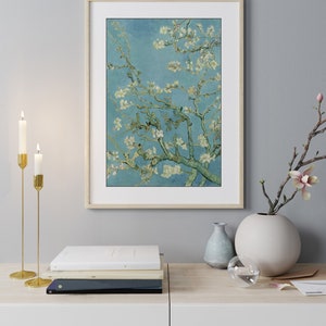May include: A framed print of a painting of a blooming almond tree with white flowers against a blue sky. The print is in a light wood frame and is hanging on a light gray wall.