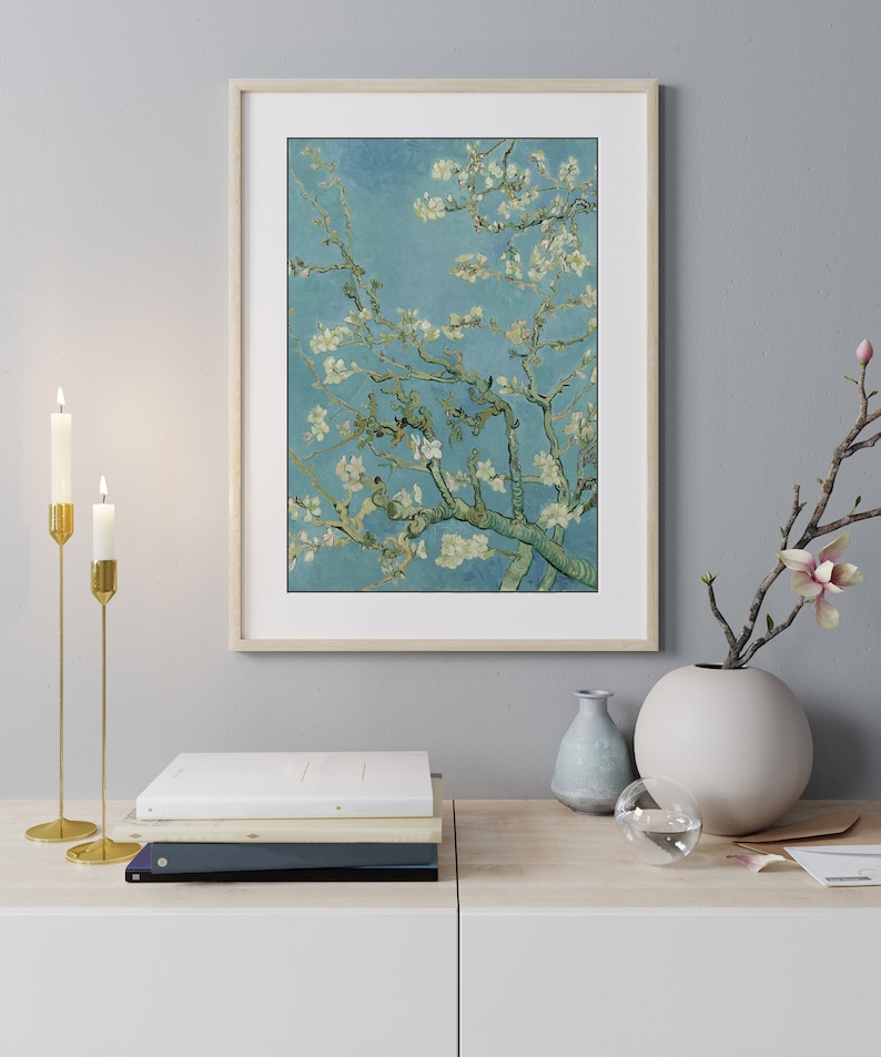 May include: A framed print of a painting of a blooming almond tree with white flowers against a blue sky. The print is in a light wood frame and is hanging on a light gray wall.