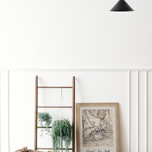 May include: A framed black and white line drawing of a street scene with the text "Vincent Van Gogh" and "Cafe Terrace at Night, 1888" below the image. The frame is on a wooden floor with a wooden ladder and two hanging plants in the background.