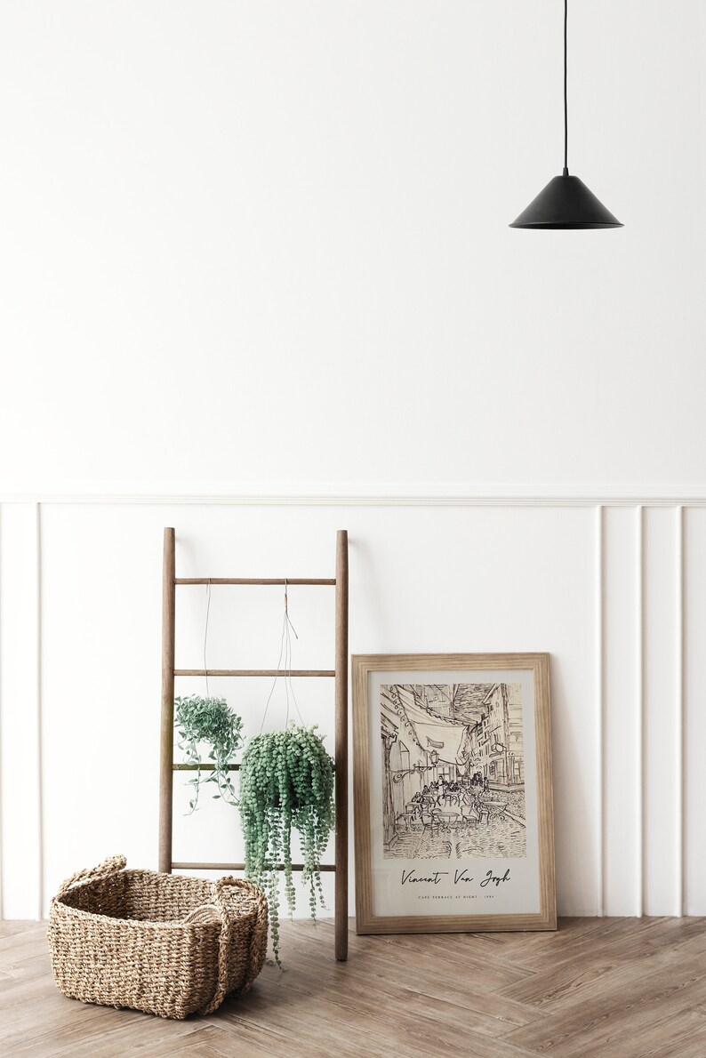 May include: A framed black and white line drawing of a street scene with the text "Vincent Van Gogh" and "Cafe Terrace at Night, 1888" below the image. The frame is on a wooden floor with a wooden ladder and two hanging plants in the background.
