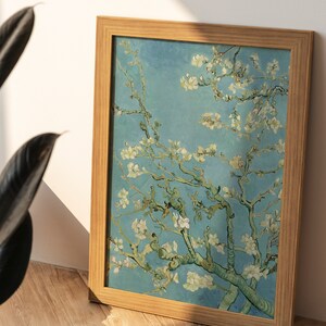 May include: A framed painting of a blooming almond tree with white flowers against a blue sky. The painting is in a light wood frame.