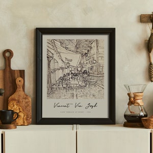 May include: A black framed print of a black and white drawing of a street scene with the text "Vincent Van Gogh, Cafe Terrace at Night, 1888". The print is hanging on a wall with a wooden shelf below it.