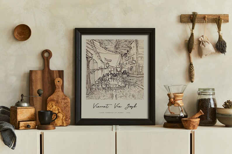 May include: A black framed print of a black and white drawing of a street scene with the text "Vincent Van Gogh, Cafe Terrace at Night, 1888". The print is hanging on a wall with a wooden shelf below it.
