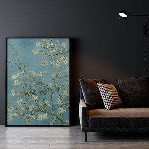 May include: A framed print of a painting depicting a branch of a flowering almond tree with white blossoms against a blue sky. The print is hanging on a dark gray wall above a dark gray couch with a black and white patterned pillow.