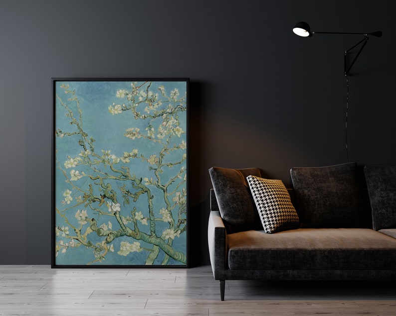 May include: A framed print of a painting depicting a branch of a flowering almond tree with white blossoms against a blue sky. The print is hanging on a dark gray wall above a dark gray couch with a black and white patterned pillow.
