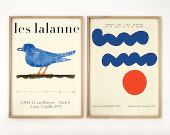 May include: Two framed posters with a minimalist design. The left poster features a blue bird with an orange beak and legs against a white background. The text "les lalanne" is at the top of the poster. The right poster features two blue wavy lines and a red circle against a cream background. The text "SEMANA DEL CINE FRANCES" is at the top of the poster.
