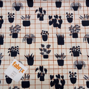 May include: A white fabric with a brown grid pattern and black silhouettes of potted plants. The fabric has the text "fabriX LANCASTER" and "make it wear it love it" printed on a white tag.