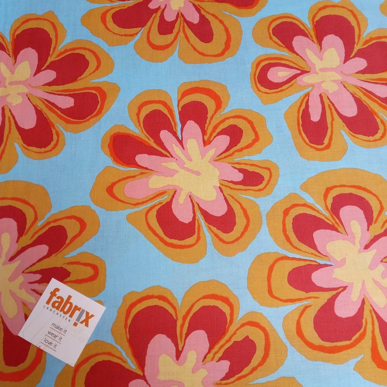 May include: A fabric with a repeating floral pattern. The flowers have red, orange, pink, and yellow petals on a light blue background. A tag in the lower left corner reads "fabrix lancaster make it wear it love it."