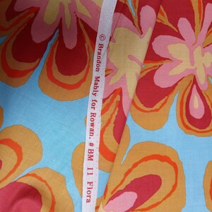 May include: Fabric with a large floral pattern in shades of red, orange, pink, and yellow on a light blue background. A white measuring tape with text that reads "&copy; Brandon Mably for Rowan. #BM 11 Flora" is visible.