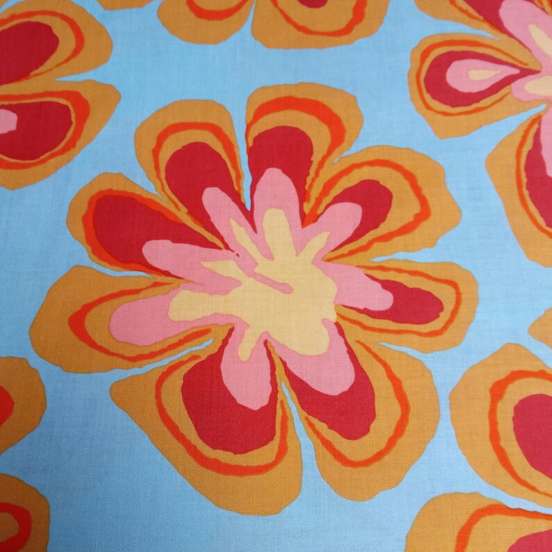 May include: A close-up of a fabric with a repeating floral pattern. The flowers have a retro design with layers of red, orange, pink, and yellow on a light blue background. The fabric has a soft, textured appearance.