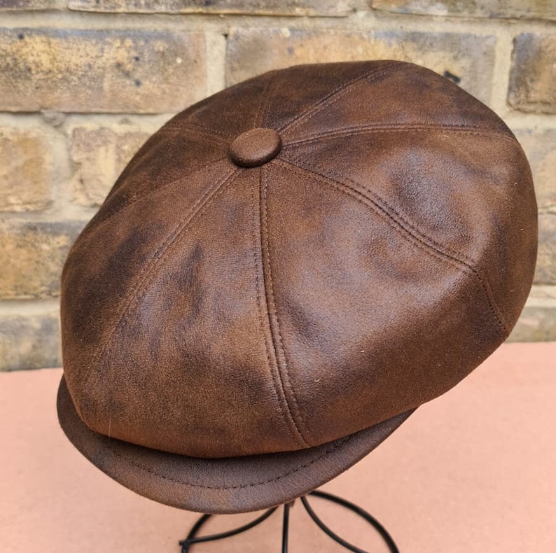 May include: A brown leather newsboy cap with a button on top. The cap has a distressed look and is made of a soft, supple leather.