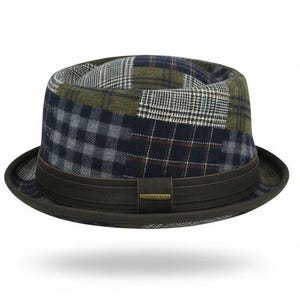 May include: A fedora hat with a patchwork design. The crown features a mix of plaid and patterned fabrics in shades of navy, olive green, and grey. A dark brown band encircles the base of the crown, with a small rectangular accent.