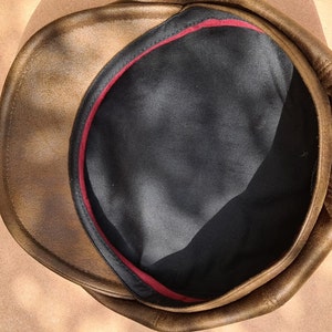 May include: A brown leather cap with a black lining and a red trim around the inside.