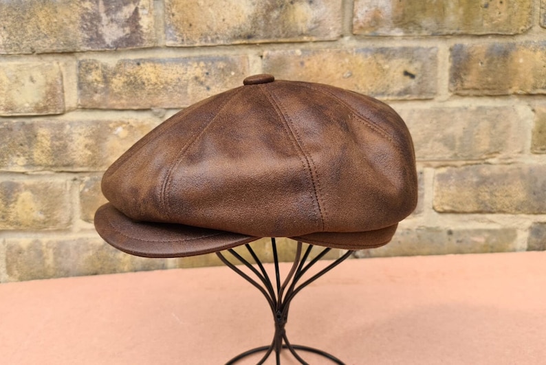 May include: A brown leather newsboy cap with a distressed finish. The cap has a rounded crown and a short brim.