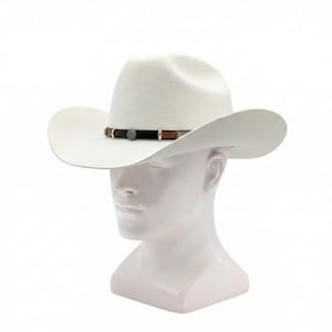 May include: A white cowboy hat with a wide brim and a decorative band. The band features black and brown leather accents, and a silver-coloured emblem. The hat is displayed on a white mannequin head.