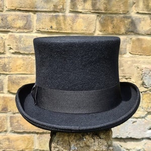 Può includere: Un cappello a cilindro nero con un nastro nero. Il cappello è fatto di feltro e ha un design classico.