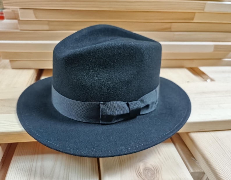 May include: A black fedora hat with a wide brim and a black ribbon with a bow.