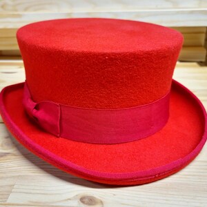 May include: A bright red top hat with a black ribbon around the base. The hat is made of felt and has a smooth, textured surface.