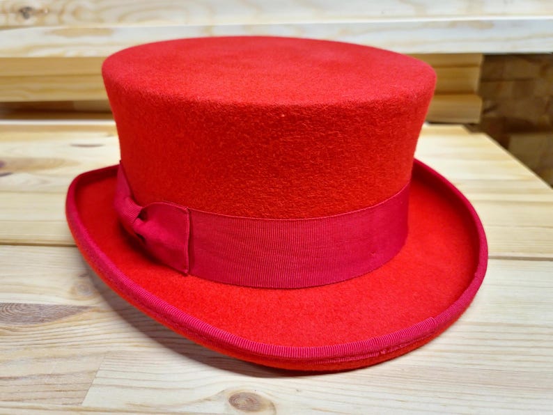 May include: A bright red top hat with a black ribbon around the base. The hat is made of felt and has a smooth, textured surface.