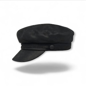May include: A black, textured leather cap with a short brim. The cap features a rounded crown, a band around the base, and a button detail on the side. The hat casts a shadow on a white background.