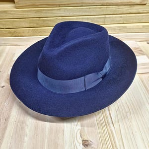 May include: A dark blue fedora hat with a wide brim and a black ribbon.
